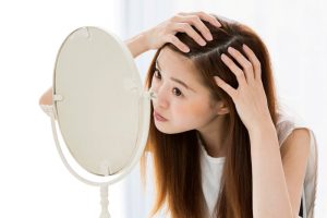 A woman looking in the mirror, concerned about her hairline transplant
